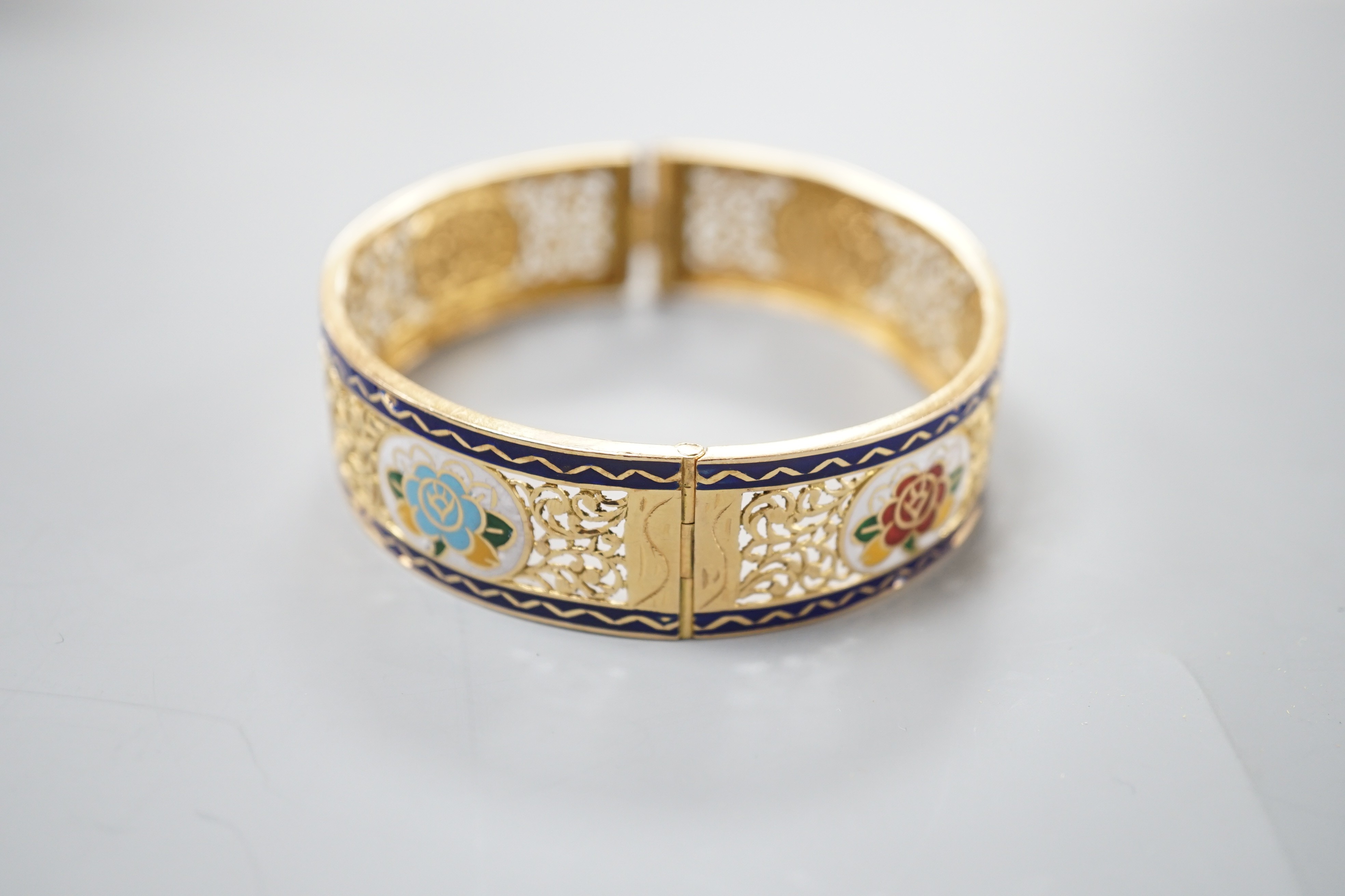 A pierced yellow metal and polychrome enamel set hinged bangle, gross weight 25.3 grams, (enamel a.f.).